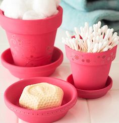 three pink pots with white flowers and cotton in them on a counter top next to folded towels