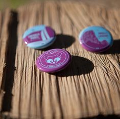 three buttons sitting on top of a wooden table next to each other and one has a cartoon character