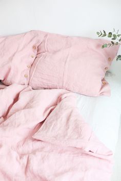 a cat laying on top of a pink bed next to two pillows and a plant