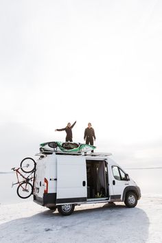 two men standing on the roof of a van with their bikes strapped to it's roof