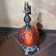 an orange vase sitting on top of a tile floor next to a light fixture with a candle in it