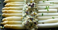 several white asparagus are lined up on a black surface with green sprinkles