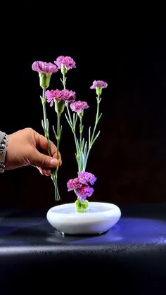 a person is arranging purple flowers in a white bowl on a black table with blue lights