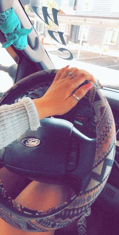 a woman driving a car with her hand on the steering wheel and wearing a knitted sweater