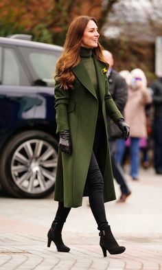 a woman in green coat and black gloves walking down the street