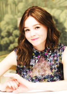 a young woman sitting at a table with her hands folded out in front of her