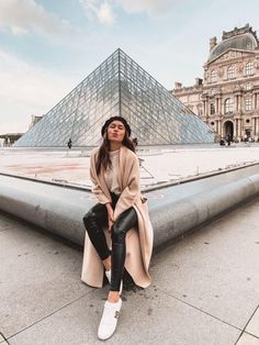 a woman sitting on the ground in front of a building with a pyramid behind her