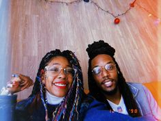 two people sitting next to each other in front of a wooden wall with lights on it