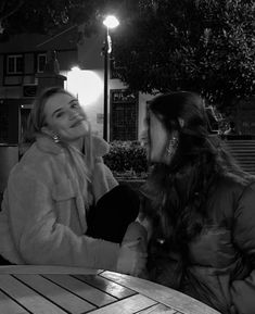 two women sitting at a table talking to each other in front of a street light