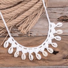 a white necklace with shells hanging from it's side on a piece of wood