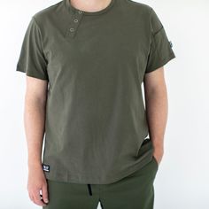 The Essential Everyday Henley Shirt Our core workwear Henley Tee is now available in a new color: Olive. This versatile tee features an apron neck tab and sleeve pocket, making it a practical choice for kitchen and service staff. Customize it with logos to impress, or let its understated silhouette make a statement on its own. Crafted from 100% premium cotton sourced from China, this tee offers substantial quality in the classic new Olive color. Pair it with the Olive Essentials Pants for a cohe Green Short Sleeve T-shirt For Work, Khaki Tops With Side Pockets For Work, Cotton T-shirt With Pockets For Work, Green Crew Neck T-shirt For Work, Green Short Sleeve T-shirt With Side Pockets, Green Cotton T-shirt With Side Pockets, Khaki Crew Neck T-shirt With Pockets, Crew Neck Top With Side Pockets For Workwear, Essentials Pants