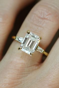 a woman's hand holding an emerald and baguette engagement ring with three bagsuetts