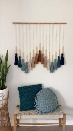 a wall hanging with tassels on it next to a chair and potted plant