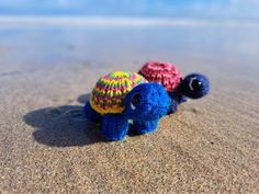 two small crocheted turtle toys laying on the sand