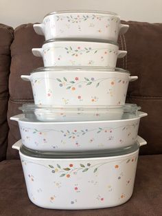 four white casserole dishes stacked on top of each other with flowers painted on them