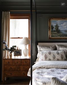 a bed sitting under a window next to a dresser with a lamp on top of it