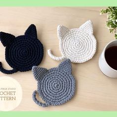 three crocheted cat coasters sitting on top of a table next to a cup of coffee