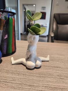 a small white vase with a plant in it on top of a table next to a pen holder