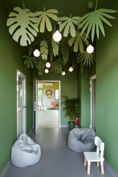 a room with green walls and white chairs on the floor next to large palm leaves hanging from the ceiling