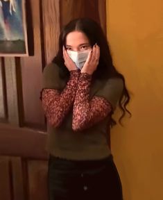 a woman wearing a face mask covering her mouth while standing in front of a door