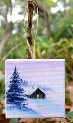 an ornament hanging from a tree branch with a painting of a cabin in the snow