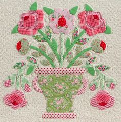 a vase filled with pink flowers on top of a white quilted wall hanging ornament