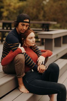 a man and woman sitting on top of a bench next to each other in front of trees