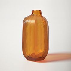 an orange glass vase sitting on top of a white table next to a shadowless wall