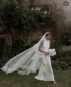 a woman in a wedding dress and veil standing on the grass with her hand over her shoulder