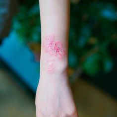 a woman's arm with a pink flower tattoo on her left wrist and right hand