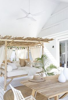 an outdoor living area with white furniture and wooden tables, including a canopy bed that has curtains over it