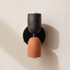 two black and orange vases are hanging on a white wall next to a light fixture