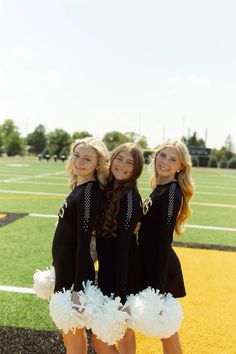 three girls in cheerleader outfits standing on a football field