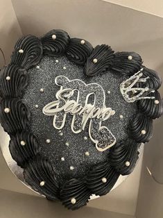 a black heart shaped cake with white frosting and writing on the top, in a box