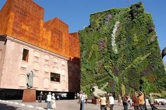 people are standing in front of a building with a green wall on it's side