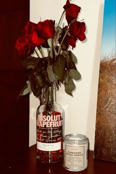 a vase filled with red roses sitting on top of a table next to a candle