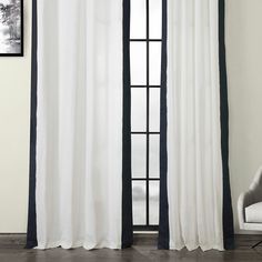 a white and black curtain hanging on a wall next to a chair in front of a window