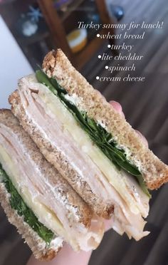 a hand holding a sandwich with meat, cheese and spinach on toasted bread