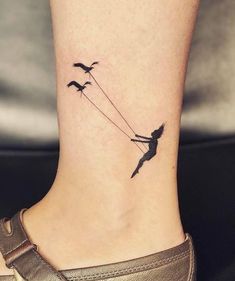 a small tattoo on the ankle of a girl with two birds flying over her head