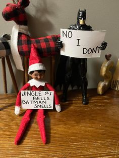 an elf is holding a sign in front of two other toy figurines on a table