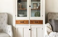 a white china cabinet sitting in the corner of a living room next to a chair