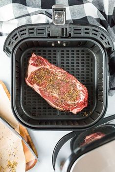 a piece of raw meat is in the air fryer next to other cooking utensils