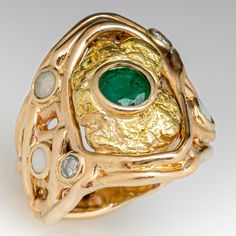 This awesome 14K yellow gold organic, freeform style ring is centered with an 18K yellow gold nugget with a bezel set, round mixed cut emerald, weighing 0.71 carats, in the middle. The shoulders are accented with a total of three (3) round, opal cabochons and two (2) round brilliant cut diamonds in bezel settings. The ring measures 23.8mm at the top, rises 4.7mm above the finger, tapering to 5.5mm wide and 22.1mm thick at the base of the shank. This ring is currently a size 7.5. The emerald show Unique Green Emerald Ring In 14k Gold, Unique 14k Gold Green Emerald Ring, Unique 14k Gold Emerald Ring, Unique Green Emerald 14k Gold Ring, Unique Yellow Gold Emerald Ring With Bezel Setting, Unique Gold Emerald Ring Birthstone, Unique Emerald Ring In 14k Gold, Unique Gold Emerald Ring With Bezel Setting, Gold Nugget