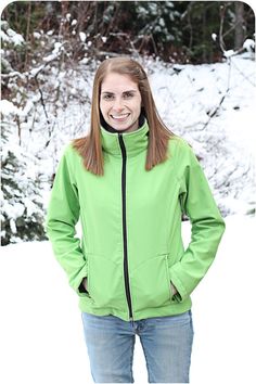 a woman standing in the snow with her hands on her hips, wearing a green jacket