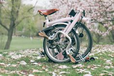 a pink bicycle is parked in the grass near some trees and leaves on the ground