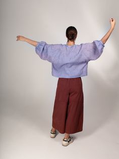 a woman in purple shirt and brown pants with her arms spread out to the side