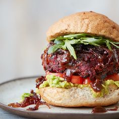 a burger with meat, lettuce and tomato on a bun sitting on a plate