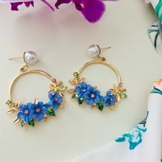 These Stunning Hoop Earrings Showcase A Vibrant Floral Design, With Delicate Blue Flowers Adorned With Pink And Green Crystals. The Golden Hoops Are Accented With Elegant Leaf Details And Are Topped With A Lustrous Pearl Stud, Adding A Touch Of Sophistication. These Earrings Are Perfect For Those Who Love Bold And Colorful Accessories, Making Them A Beautiful Statement Piece For Both Casual And Formal Occasions. Their Playful Yet Refined Style Is Sure To Bring A Fresh And Lively Vibe To Any Outfit. Blue Spring Earrings, Blue Spring Earrings For Pierced Ears, Spring Party Blue Jewelry, Blue Jewelry For Summer Party, Blue Summer Jewelry For Party, Summer Blue Jewelry For Party, Blue Summer Party Jewelry, Blue Flower Earrings For Party, Summer Jewelry With 3d Flower Shapes