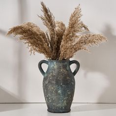 a vase with some dried plants in it on a table next to a white wall