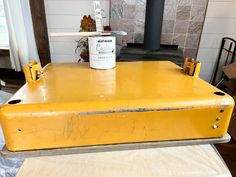 an old yellow suitcase with a paint can on it sitting in front of a fireplace